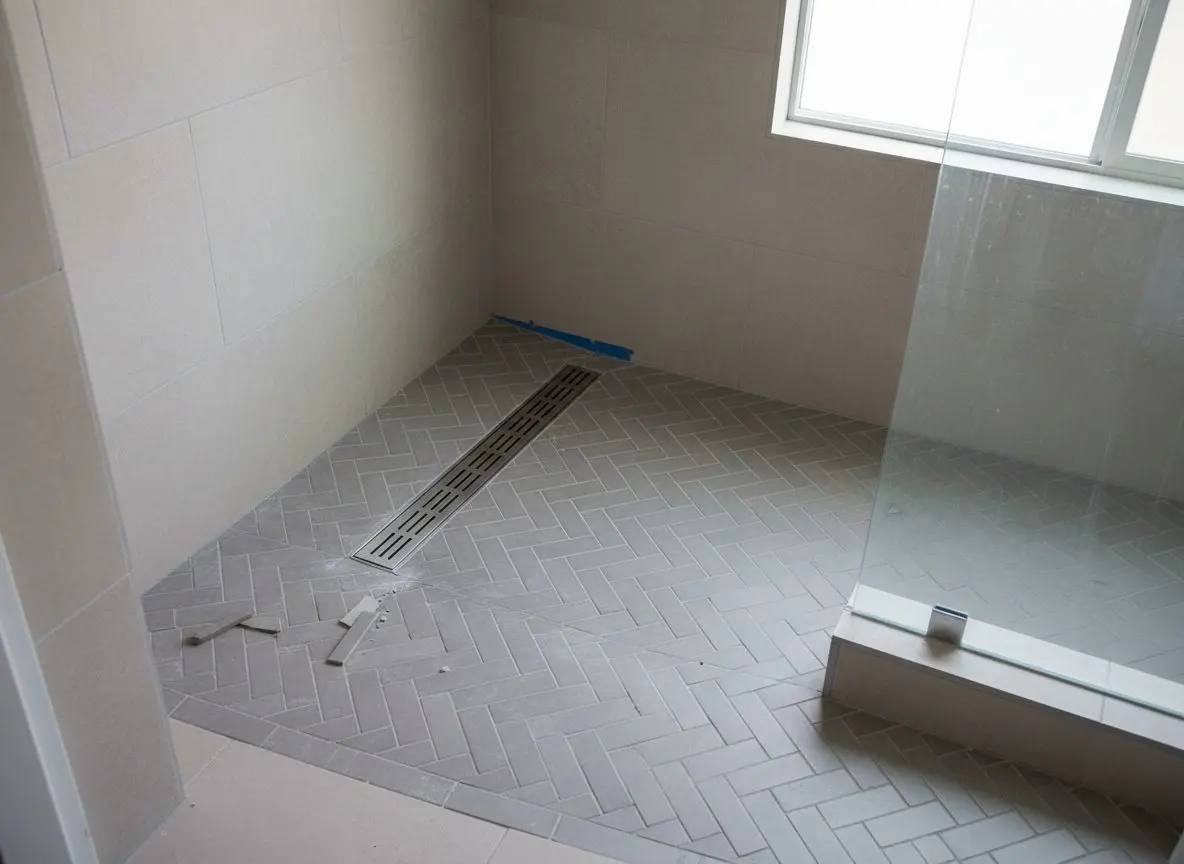 The sloped tile floor of a curbless shower meeting a slim linear drain at the low edge.