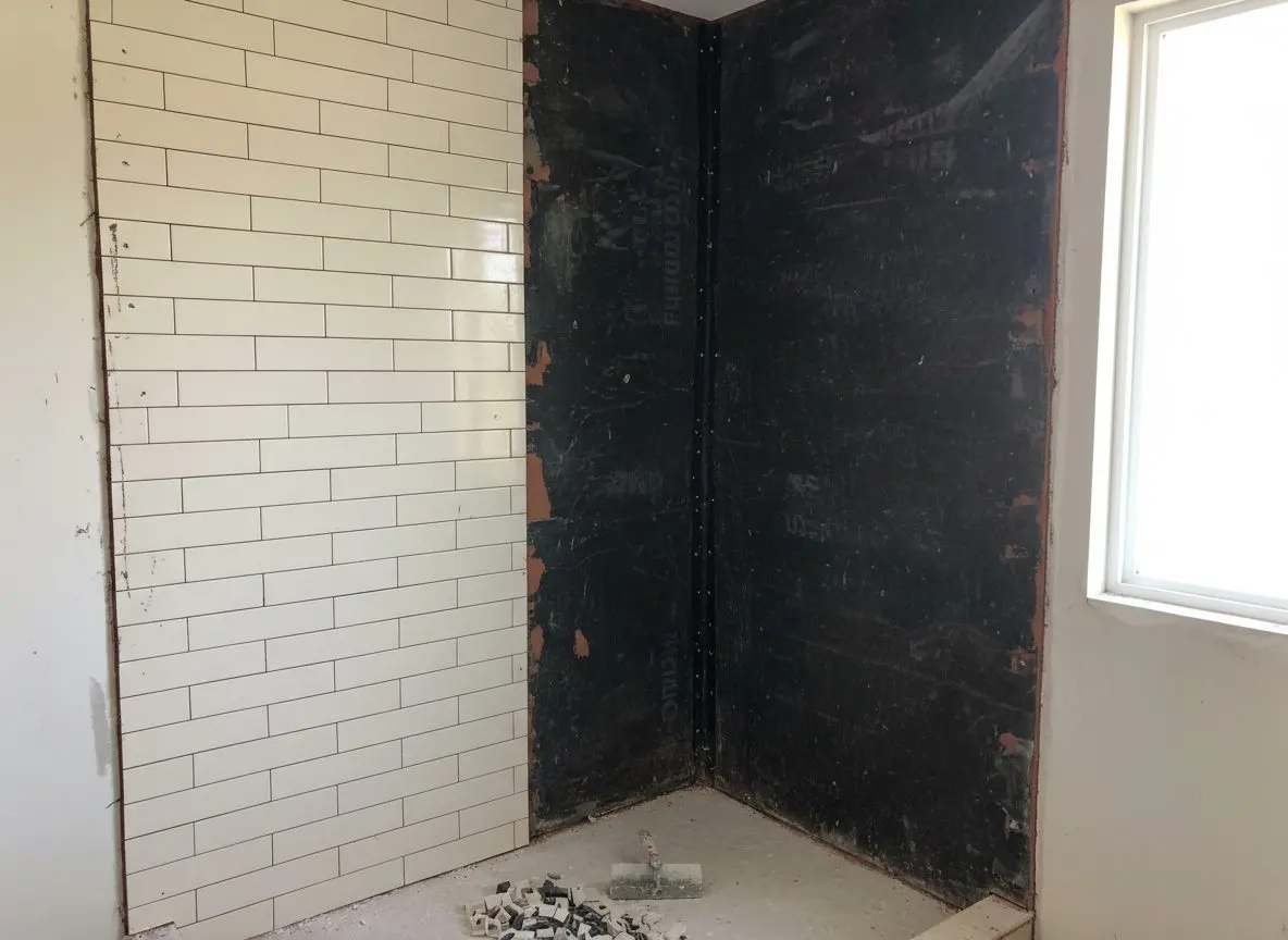 A half-finished shower conversion, tile set on one wall and the waterproofing membrane still exposed on the other two.